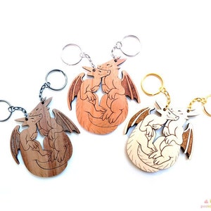 May include: Three wooden dragon keychains with silver and gold key rings. The dragons are in a curled up position with their tails intertwined. The dragons are in different shades of brown.