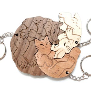 Op de afbeelding: Houten katvormige sleutelhangers in verschillende bruin- en beigetinten. Elke sleutelhanger heeft een ander kattenontwerp, verbonden door zilveren kettingen en sleutelringen. De sleutelhangers zijn in een cirkelvorm gerangschikt.