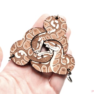 Peut inclure: Un porte-cl&eacute;s en bois avec un motif de serpent brun et blanc. Le serpent est repr&eacute;sent&eacute; enroul&eacute;, avec sa t&ecirc;te et sa queue visibles. Le porte-cl&eacute;s est en bois d&eacute;coup&eacute; au laser et poss&egrave;de un anneau m&eacute;tallique pour attacher les cl&eacute;s.