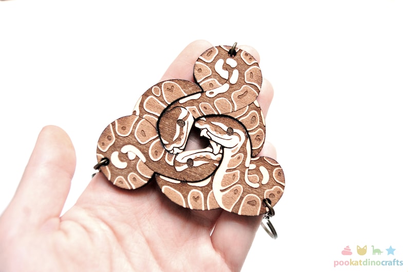Peut inclure: Un porte-cl&eacute;s en bois avec un motif de serpent brun et blanc. Le serpent est repr&eacute;sent&eacute; enroul&eacute;, avec sa t&ecirc;te et sa queue visibles. Le porte-cl&eacute;s est en bois d&eacute;coup&eacute; au laser et poss&egrave;de un anneau m&eacute;tallique pour attacher les cl&eacute;s.