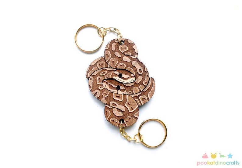 May include: A brown and white snake keychain with a gold key ring. The snake is curled up in a knot and has a realistic pattern.