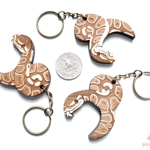 Peut inclure: Trois porte-cl&eacute;s en bois en forme de serpent avec un motif blanc et brun. Chaque porte-cl&eacute;s a un anneau et une cha&icirc;ne en m&eacute;tal.