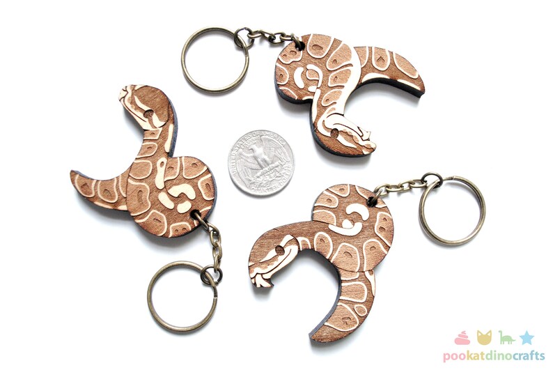 Peut inclure: Trois porte-cl&eacute;s en bois en forme de serpent avec un motif blanc et brun. Chaque porte-cl&eacute;s a un anneau et une cha&icirc;ne en m&eacute;tal.