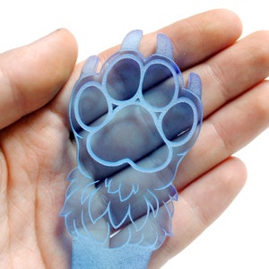 May include: A blue paw print charm with a furry design. The charm is made of acrylic and has a translucent finish.