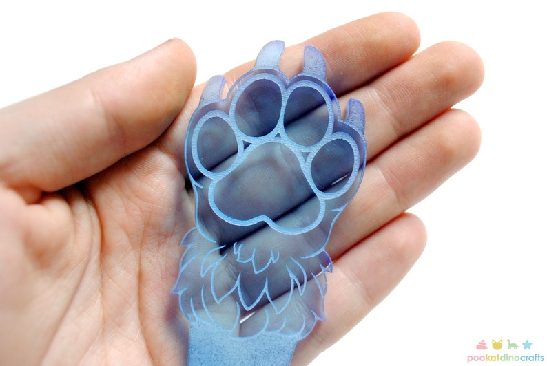 May include: A blue paw print charm with a furry design. The charm is made of acrylic and has a translucent finish.