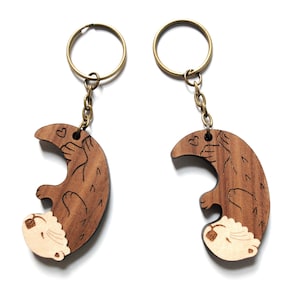 May include: Two wooden keyrings shaped like otters holding hearts. The otters are brown with white faces and are attached to gold key rings.