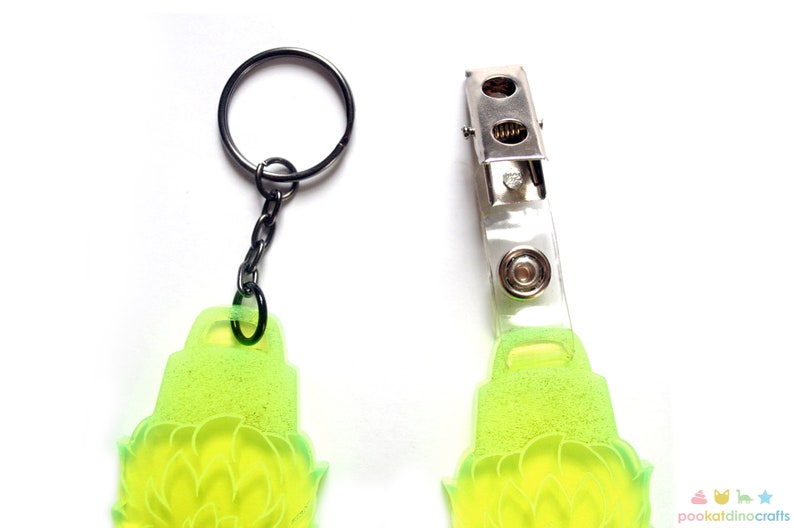 May include: A lime green keychain with a floral design. The keychain has a metal ring and a clear plastic badge holder with a metal clip.