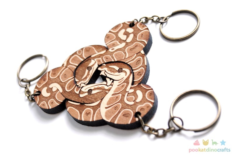 Peut inclure: Un porte-cl&eacute;s en bois avec un motif de serpent brun et blanc. Le porte-cl&eacute;s a trois anneaux.