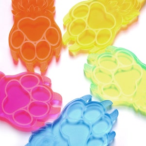 May include: Five colorful paw print keychains made of clear plastic. The keychains are in shades of orange, yellow, green, pink, and blue. Each keychain has a paw print design with three toes and a small, stylized tail.