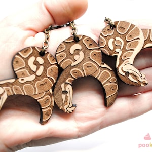 Peut inclure: Trois porte-cl&eacute;s en bois en forme de serpent avec un motif brun et blanc. Les porte-cl&eacute;s sont attach&eacute;s &agrave; une cha&icirc;ne en m&eacute;tal.