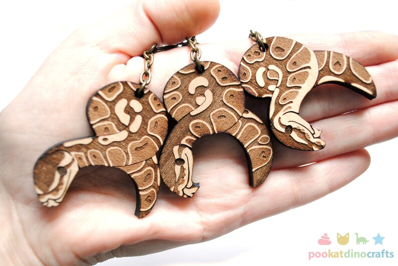 Peut inclure: Trois porte-cl&eacute;s en bois en forme de serpent avec un motif brun et blanc. Les porte-cl&eacute;s sont attach&eacute;s &agrave; une cha&icirc;ne en m&eacute;tal.