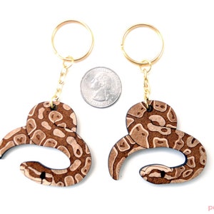 May include: Two brown and white snake-shaped keychains with gold key rings and chains. The keychains are about the size of a US quarter.