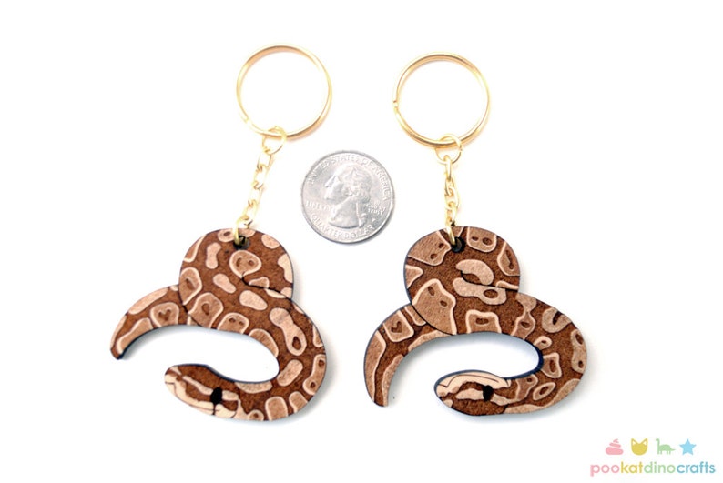 May include: Two brown and white snake-shaped keychains with gold key rings and chains. The keychains are about the size of a US quarter.