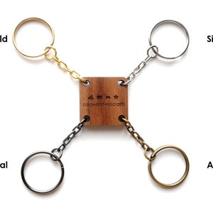 May include: Four keychains in different finishes: gold, silver, gunmetal, and antique. Each keychain is attached to a wooden square with the text "oookaladinocrafts" engraved on it.