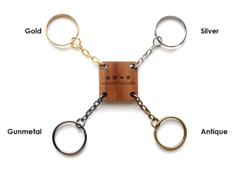 May include: Four keychains in different finishes: gold, silver, gunmetal, and antique. Each keychain is attached to a wooden square with the text "oookaladinocrafts" engraved on it.