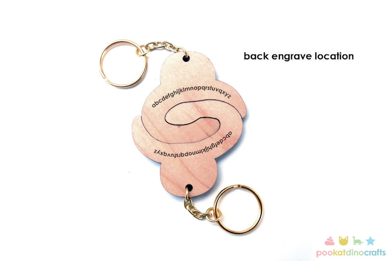 May include: Wooden alphabet keychain with a spiral design. The keychain is made of natural wood and features the letters of the alphabet in a spiral pattern. The back of the keychain has a blank space for engraving.