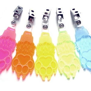May include: Five colorful plastic paw print keychains with metal clips. The paw prints are in shades of pink, orange, yellow, light yellow, and blue.