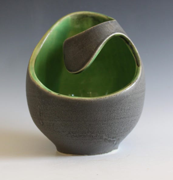 A hand-thrown ikebana vase in moody charcoal and green glaze — the kind of modern ceramic that makes a single stem look like it belongs in a gallery.