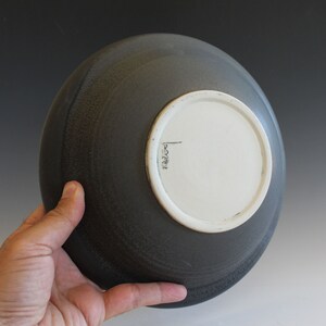 May include: A dark gray ceramic bowl with a white glazed bottom. The bowl has a slightly textured surface and a simple, rounded shape.