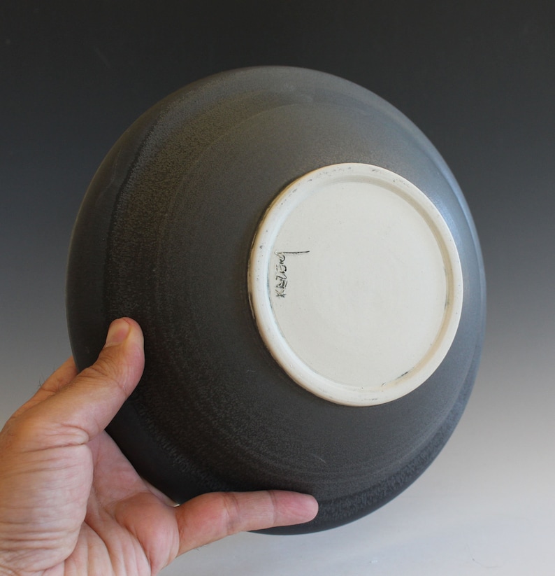 May include: A dark gray ceramic bowl with a white glazed bottom. The bowl has a slightly textured surface and a simple, rounded shape.