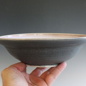 May include: A gray ceramic bowl with a light pink interior. The bowl has a slightly rounded shape and a textured exterior.