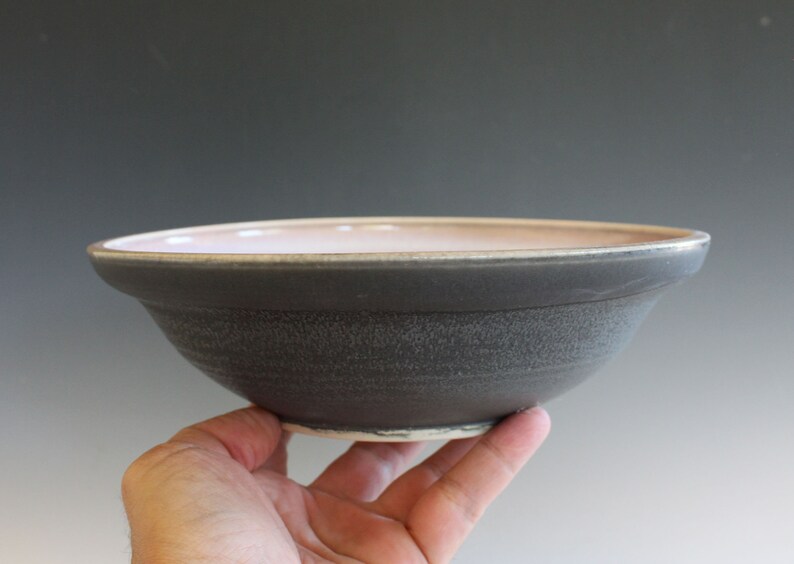 May include: A gray ceramic bowl with a light pink interior. The bowl has a slightly rounded shape and a textured exterior.