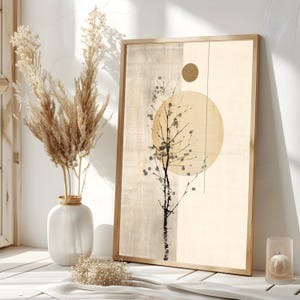 May include: A framed abstract art print featuring a tree silhouette with a large yellow circle and a smaller gold circle. The artwork has a neutral color palette with beige and cream tones. A white vase with dried pampas grass and a candle in a glass holder are in the foreground.