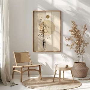 May include: A framed art print featuring a minimalist design with a tree silhouette and a large yellow circle. The artwork is in a wooden frame and hangs above a chair and a small stool. The color palette is neutral with beige and brown tones.