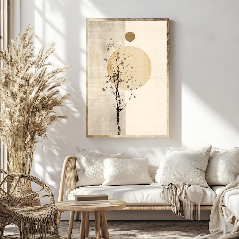 May include: Framed abstract art print featuring a stylized tree silhouette against a beige and cream background with a large yellow circle and a smaller gold circle. The artwork is displayed above a wicker sofa with white pillows.