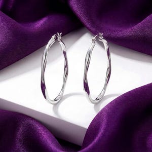May include: A pair of silver-toned hoop earrings featuring a distinct twisted, wavy metal design. The earrings have a polished, reflective surface and a secure hinged closure mechanism, presenting a clean and metallic aesthetic for jewelry.