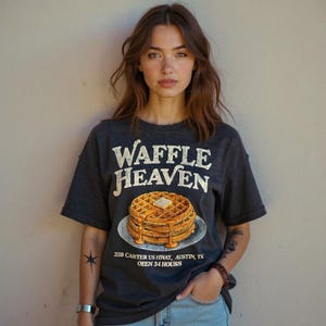 May include: Dark gray t-shirt with the text "Waffle Heaven" above a graphic of waffles with syrup. The shirt also includes the address "238 Carter US Hwy, Austin, TX" and "OPEN 24 HOURS".