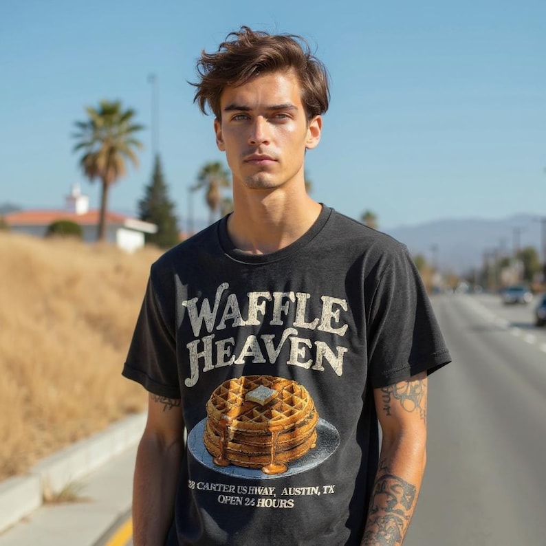 May include: Black t-shirt with the words "Waffle Heaven" in a distressed font. Below the text is an illustration of a stack of waffles with butter and syrup. The shirt also includes the address "Carter US Hwy, Austin, TX" and "Open 24 Hours."