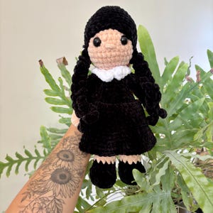 Può includere: Bambola all'uncinetto fatta a mano con capelli neri in due trecce, indossa un vestito nero con colletto bianco. La bambola ha un viso color pesca chiaro e occhi neri. La bambola è alta circa 25 cm.