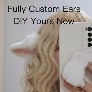 Puede incluir: Orejas de animal de piel sintética blanca unidas a una diadema, usadas con cabello rubio ondulado. Un teléfono inteligente blanco presenta un agarre transparente en forma de conejo en la parte posterior. El texto "Fully Custom Ears" y "DIY Yours Now" es visible en la parte superior.