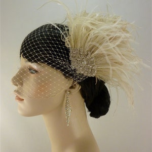 May include: A white feather bridal hairpiece with a crystal embellishment and a birdcage veil. The hairpiece is worn on a mannequin with long, dark hair.