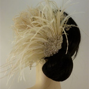 May include: A white feather hair comb with a large, sparkly rhinestone embellishment. The comb is worn in a woman's hair, which is styled in a bun.