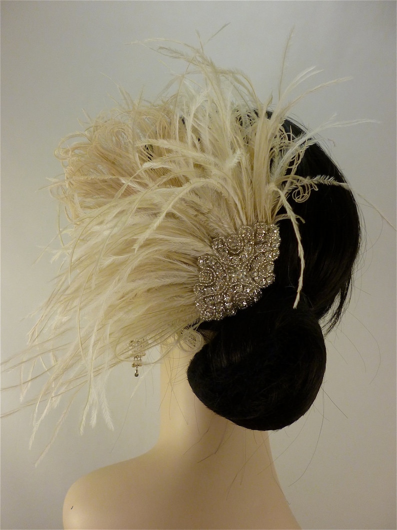May include: A white feather hair comb with a large, sparkly rhinestone embellishment. The comb is worn in a woman's hair, which is styled in a bun.