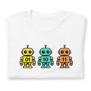Könnte beinhalten: Weißes T-Shirt mit drei Cartoon-Robotern in Gelb, Türkis und Orange. Jeder Roboter hat eine andere Nummer: 01, 10 und 11. Die Roboter haben schwarze Umrisse und Antennen. Das T-Shirt ist gefaltet.