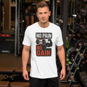 May include: White t-shirt with the text "NO PAIN NO GAIN" in black and red, along with a barbell and flexing arm graphic. The shirt is worn by a person in a gym setting.