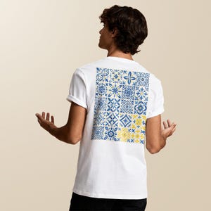 Peut inclure: T-shirt blanc avec un motif de carreaux carrés au dos. Le motif présente des motifs floraux et géométriques bleus et jaunes. Le t-shirt a des manches courtes et un col rond.