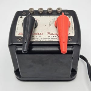 Peut inclure: Un transformateur Multi-Control Lionel Corporation Type 1033 noir de 90 watts, doté d'un panneau de commande blanc avec des leviers noir et rouge, quatre bornes métalliques et du texte imprimé incluant 115 volts, 60 cycles et Made in U.S. of America.