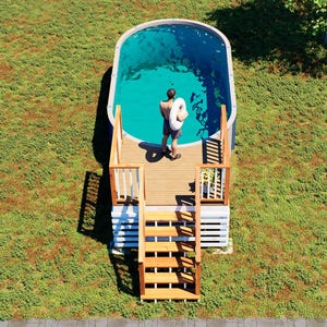 May include: An oval above-ground swimming pool with a wooden deck and staircase. The pool features blue water and is surrounded by a grassy lawn with trees. The text BAMBOO DESIGNS Home Plans & Designs is visible in the bottom left corner of the image.
