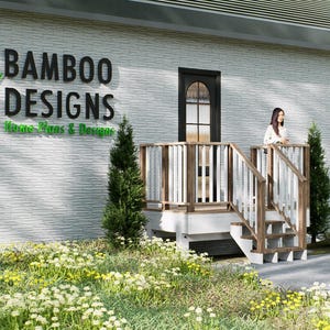 以下が含まれることがあります： 黒と緑の「BAMBOO DESIGNS」の文字が入った建物の外観。女性が手すりのある木製のポーチに立っています。建物は明るい灰色のテクスチャード加工されたファサードと濃い灰色の屋根があります。造園には小さな木と花の咲く植物が含まれています。