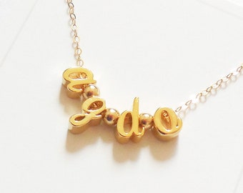 Könnte beinhalten: Goldkette mit dem Wort "I do" in kursiv geschriebenen Buchstaben. Die Buchstaben sind durch kleine goldene Perlen verbunden.