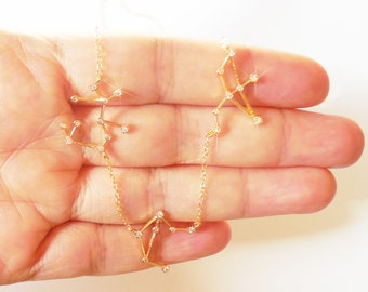 May include: A gold chain necklace with a constellation design featuring small clear stones. The necklace is displayed on a hand.