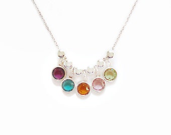 May include: A silver chain necklace with seven dangling charms. Each charm features a round, faceted gemstone in a different color: pink, green, orange, turquoise, purple, yellow, and light green.