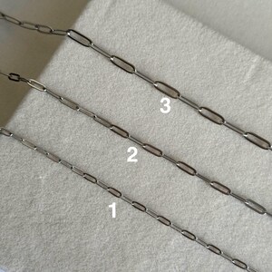 May include: Three silver-colored paperclip chain necklaces, each with a different link size, are displayed diagonally. The chains are numbered 1, 2, and 3. The background is a light gray fabric.