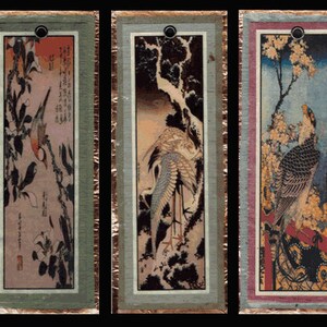 May include: Set of three rectangular bookmarks featuring Japanese-style art prints. Each bookmark has a different image of a bird, with a decorative border and a hole at the top. The artwork includes birds, branches, and text.