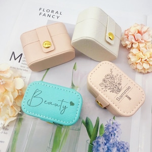 May include: Four small, pastel-colored jewelry boxes. Two are square with a snap closure and gold button. One is light blue with the word "Beauty" and a heart. The fourth is beige with a floral design and the name "Sammie".