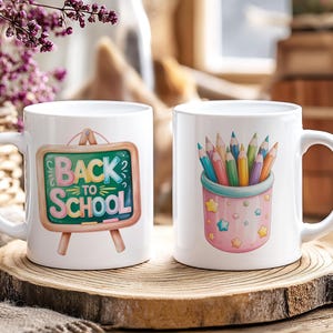 Puede incluir: Dos tazas de cer&aacute;mica blanca con dise&ntilde;os escolares. Una taza presenta una pizarra con el texto "BACK TO SCHOOL". La otra taza muestra un portal&aacute;pices lleno de l&aacute;pices de colores. Ambas tazas est&aacute;n sobre una superficie de madera.